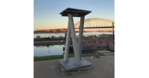 Skulptur am Ufer mit Fluss und Brücke im Hintergrund bei Sonnenuntergang