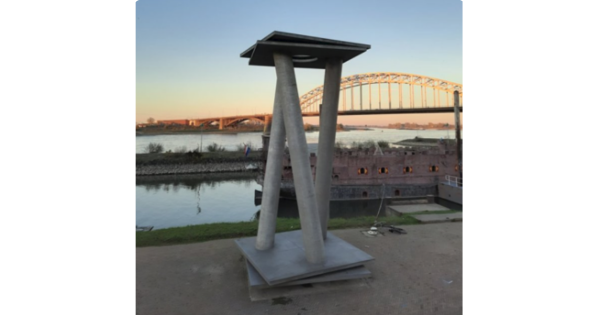 Skulptur am Ufer mit Fluss und Brücke im Hintergrund bei Sonnenuntergang