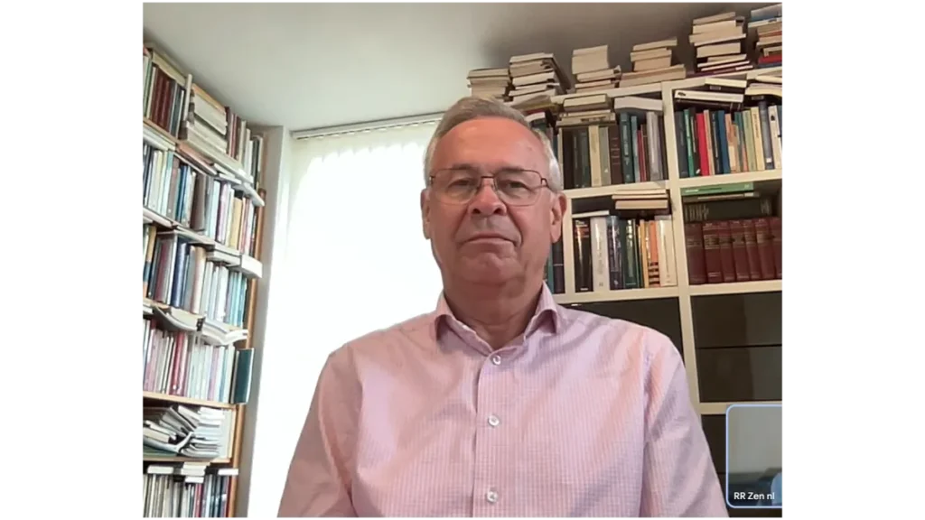Porträtfoto von Zen-Lehrer Jan Brok. Er sitzt vor zwei großen, vollgepackten Bücherregalen und blickt mit einem ruhigen Ausdruck in die Kamera.