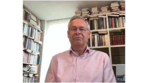 Porträtfoto von Zen-Lehrer Jan Brok. Er sitzt vor zwei großen, vollgepackten Bücherregalen und blickt mit einem ruhigen Ausdruck in die Kamera.