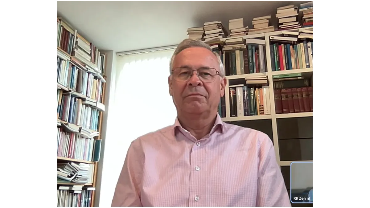 Porträtfoto von Zen-Lehrer Jan Brok. Er sitzt vor zwei großen, vollgepackten Bücherregalen und blickt mit einem ruhigen Ausdruck in die Kamera.